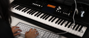Image shows a student working with a computer and keyboard in a music class